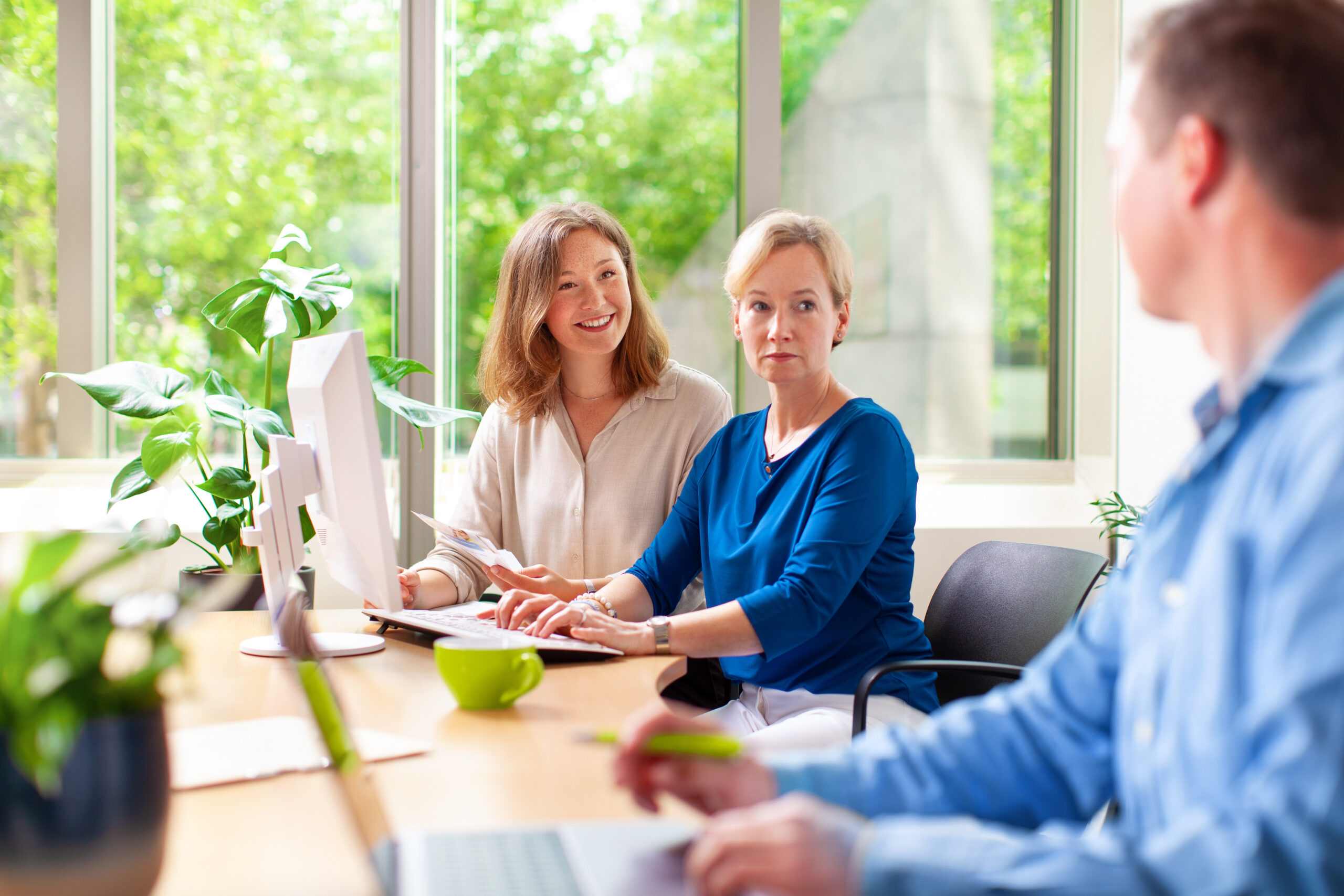 Zwei lächelnde Mitarbeiterinnen schauen zu einem Kollegen.