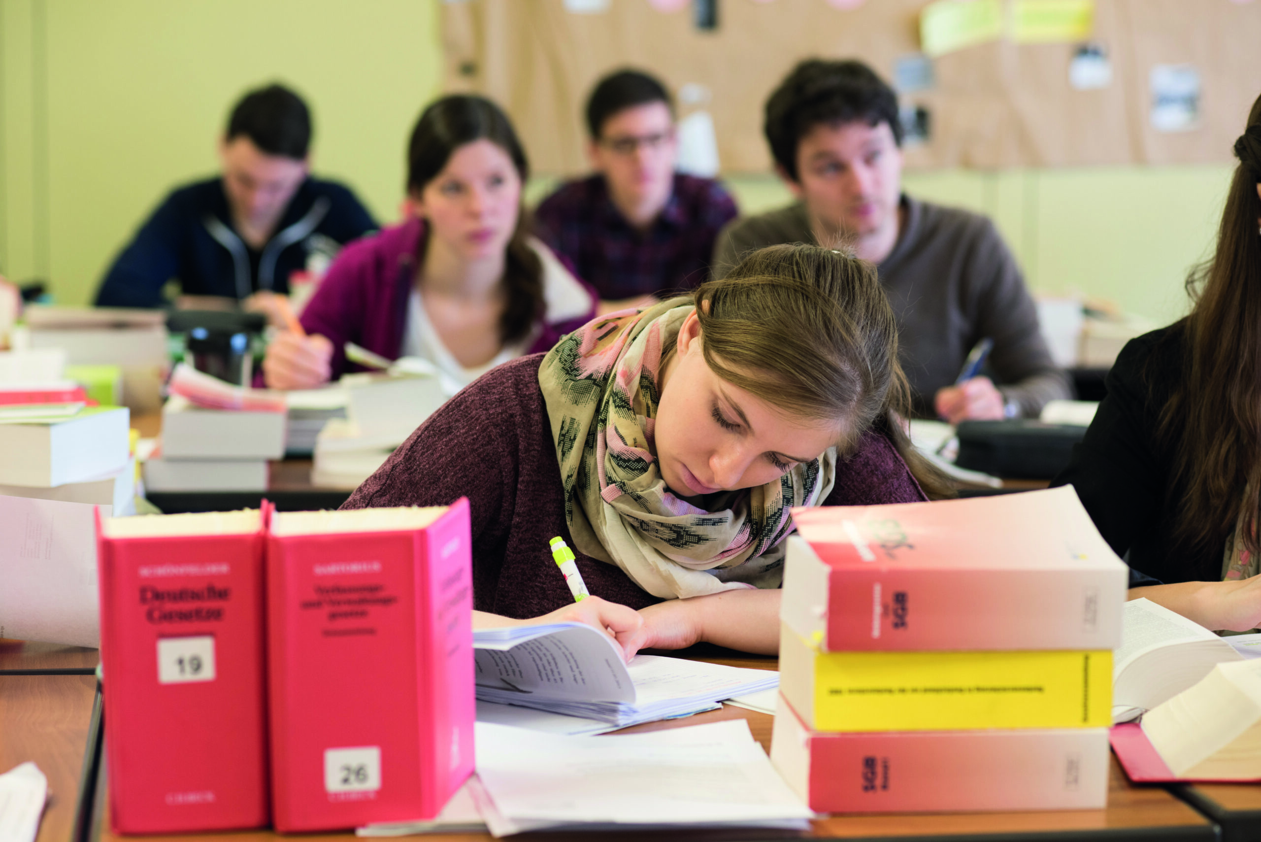 eine konzentrierte Studentin/Auszubildende schreibt etwas, während sich auf ihrem Schreibtisch Gesetzesbücher stapeln.
