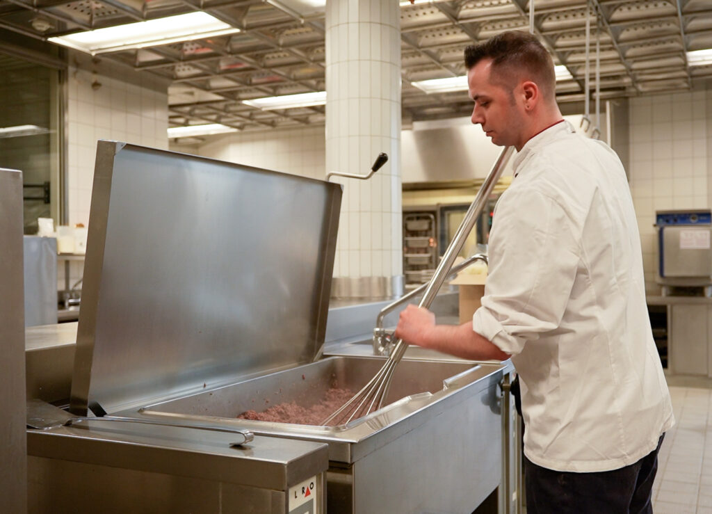 Ein Koch steht in einer Großküche und bereitet Essen zu.